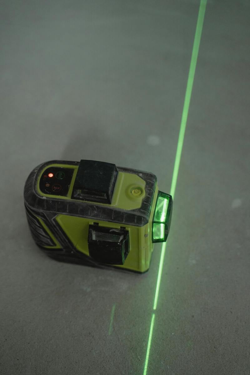 Grön laserpass på ett betonggolv som markerar en rak linje för mätning och byggarbete.