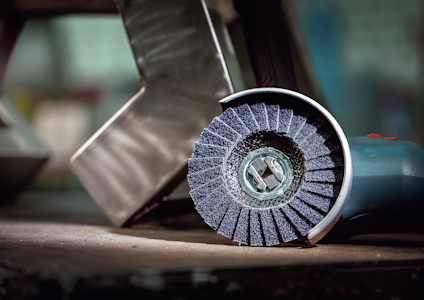 Vinkelslip med blå lamellrondell, stålrör i bakgrunden.