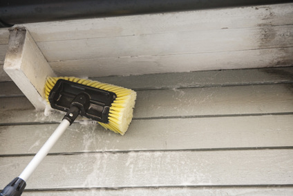 Gul borste med skaft används för att tvätta vitmålat takutsprång och grå träfasad.