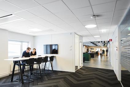 Personer sitter vid ett högt bord i ett modernt kontorsutrymme med glasväggar.