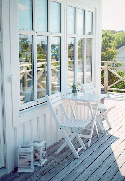 Vit uteplats med två stolar och ett bord framför stora fönster. Lanternor står på trägolvet.