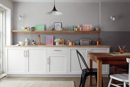 Modernt kök med vita skåp, träbord, hylla med dekorationer, och vägglampor. Svart taklampa och fönster till vänster.