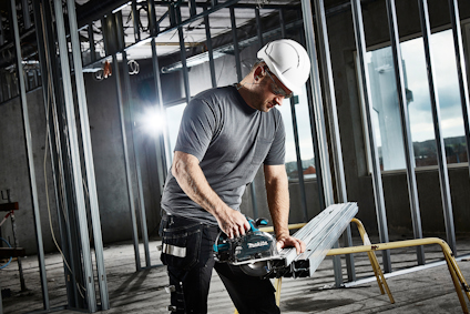 Person i hjälm och arbetskläder använder en cirkelsåg på stålrör i en byggarbetsmiljö.