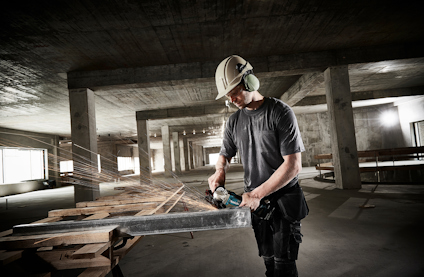 Person med skyddsutrustning använder en motorsåg för att skära genom en stor träbjälke i en industribyggnad.