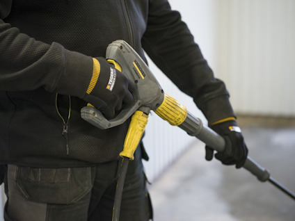 Person håller i en högtryckstvätt med gul och svart handtag, bär handskar och mörka kläder.