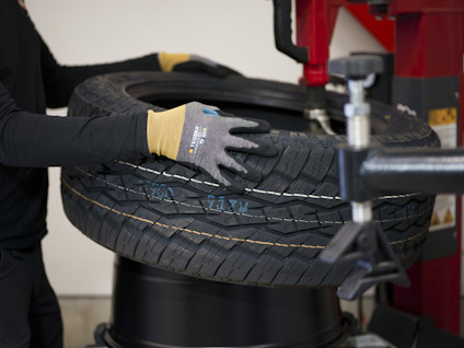 En person med handskar installerar ett bildäck på en maskin.