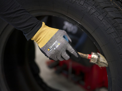 Hand med handske applicerar substans på ett bildäck med pensel.