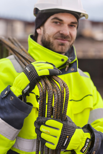 En person i skyddshjälm och reflexjacka håller buntar av armeringsjärn med handskar.