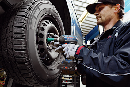 En person i arbetskläder använder en elektrisk mutterdragare för att skruva på ett bildäck i en verkstad.