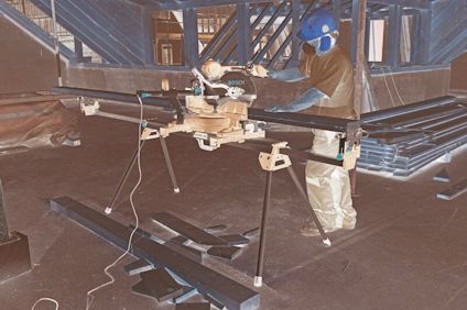 Person såg med bordssåg på en byggarbetsplats, omgiven av träbjälkar och osågat virke.