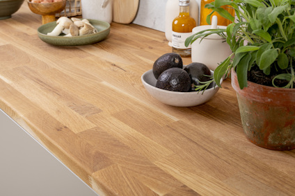 Träbänkskiva med svart avokado i en skål, grön växt i kruka och kryddflaska i bakgrunden.