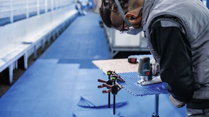 Person arbetar med ett elverktyg vid ett långt transportband.