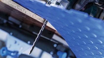 Ett sågblad skär genom en blå plastskiva med cirkulära mönster.