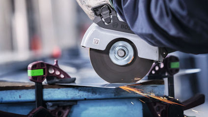 Person använder en vinkelslip för att kapa en metallbit; gnistor flyger.