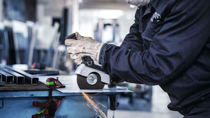 Arbetare i skyddshandskar slipar metallstycke med vinkelslip.