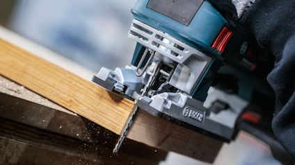 Sticksåg som sågar genom trä, sedd i närbild. Bruna träspån faller under sågningen.