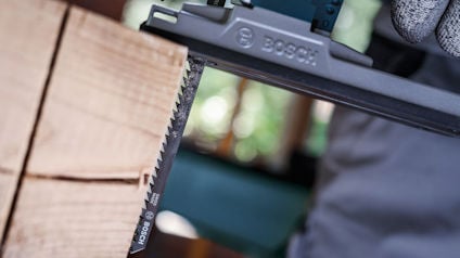 Elektrisk såg från Bosch med ett sågblad nära en trälåda. Bakgrund med oskarp inomhusmiljö.