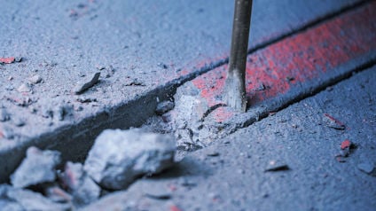 Närbild av en mejsel som knäcker betong längs en röd spraymärkt linje.