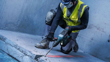 Person i skyddsutrustning använder en borrhammare för att bryta betonggolv.