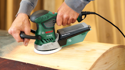 En person använder en grön och svart eldriven slipmaskin på en träyta.