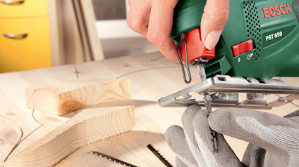 Elektrisk sticksåg, Bosch PST 650, används för att såga trä. Handskar bärs för säkerhet.