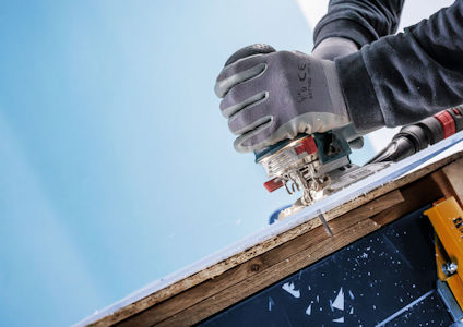 Person i handskar sågar träplanka med elektrisk såg.