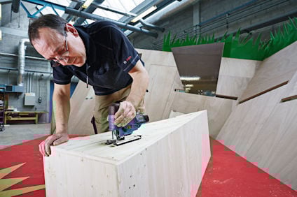 Person använder ett elektriskt verktyg på en stor träbit i en verkstad.