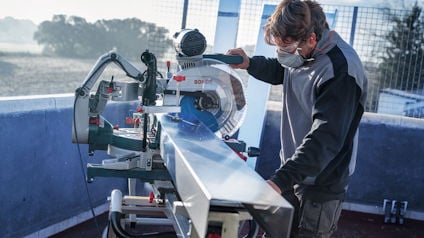 Person sågar metallbalk med en Bosch kap- och gersåg utomhus. Använder skyddsglasögon.