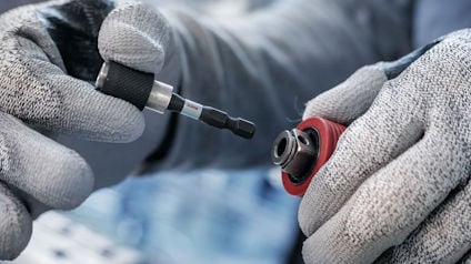 Person med gråa handskar håller en skruvdragare och en bitshållare.