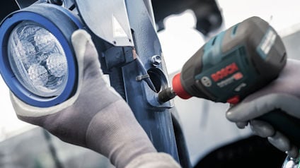 Händer i handskar monterar en fordonsstrålkastare med en elektrisk skruvdragare.