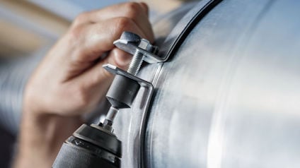 Hand som justerar bult på ett metallrör med skruvdragare.