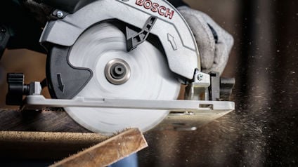 Cirkelsåg i bruk, sågar en träplanka; träflisor flyger i luften.