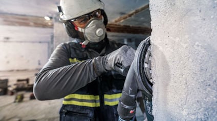 Arbetare i skyddsutrustning hanterar maskin mot betongvägg inomhus.