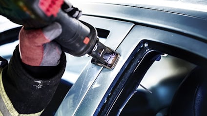 Person använder elektrisk verktyg på bilens fönsterkarm, iförd handske och jacka.