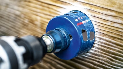 Borrmaskin med blå sågkrona borrar i träyta.