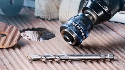 Borrskärare av metall med vriden design liggande bredvid ett borrhål i trä och borrbitsfäste.