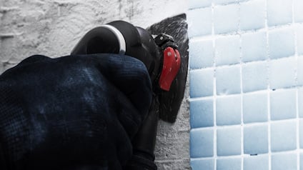 Hand i handske som använder ett verktyg för att bearbeta kakel på en vägg.