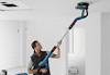 Person som använder en långskaftad slipmaskin för att slipa ett vitt tak i ett rum.