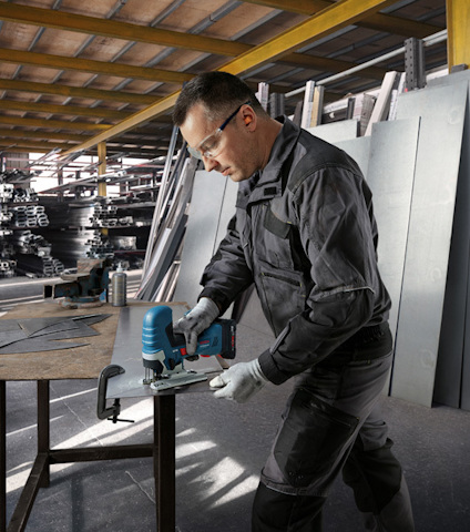 En person använder en blå sticksåg för att såga genom ett metallark i en verkstad.