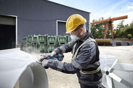 Arbetare i hjälm och skyddsutrustning använder en elektrisk verktyg på metallkonstruktion utomhus.