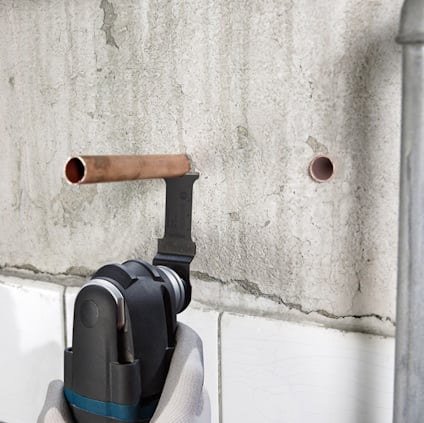 Verktyg skär en kopparrör mot en vägg med två hål.