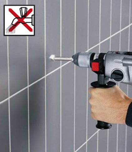 Hand som håller en borrmaskin mot kakelvägg, skylt med överkryssad borr och vatten.