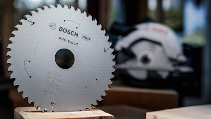 Cirkelklinga från Bosch Pro Wood med tandad kant, placerad på ett bord. En oskarp maskin i bakgrunden.