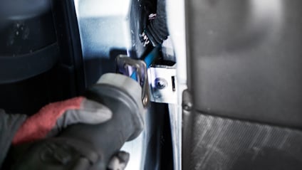 Person i röd handske använder en elektrisk såg för att skära metall i ett fordon.
