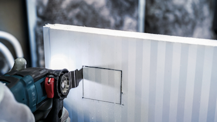 En person skär en rektangel i en styv isoleringsskiva med en elektrisk såg.